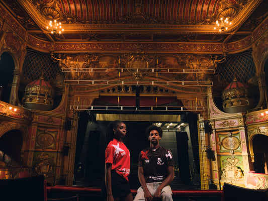 Two Hackney Women's FC players in red and black Hackney Empire jerseys on the Hackney Empire stage