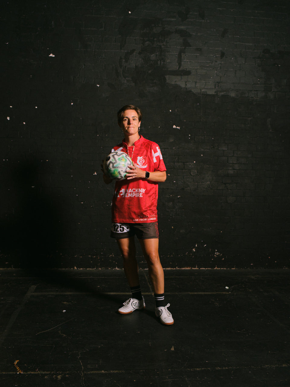 Hackney Women's FC player in the red Hackney Empire jersey, holding a match ball
